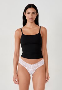 Camisola nera in rayon con spalline sottili, abbinata a perizoma bianco in pizzo con motivi floreali e bordi ondulati. Design liscio e aderente.