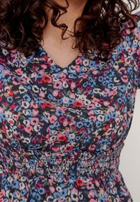 Blumenkleid mit dunkelblauem Hintergrund und pinken, blauen und roten Blumen, V-Ausschnitt und smockiertem Bund für eine figurbetonte Silhouette.