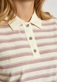 Stripet polo-shirt i creme og lys pink, med en blød tekstur, en klassisk krave og fire dekorative sølvknapper på placket.