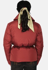 Rød dunjakke med belte i midjen, med hette og glatt tekstur. Et mønstret grønt silkeskjerf er knyttet i håret.