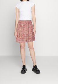 Falda de estampado floral en rosa y beige con cintura fruncida. Combinada con una blusa blanca ajustada y zapatos de plataforma negros.