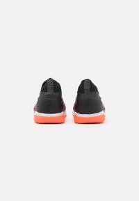 Zapatillas deportivas de malla con un vibrante degradado de púrpura a negro, talón negro y suela exterior naranja brillante. Diseño ligero con detalles texturizados.