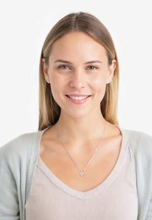 Collana in argento con pendente floreale; indossata con un cardigan grigio chiaro e un top a coste beige. Texture liscia e design delicato.