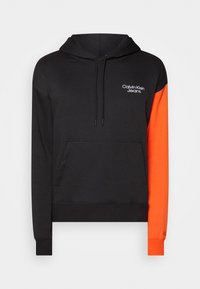 Sudadera negra con una manga naranja. Cuenta con un bolsillo frontal, capucha con cordón y logo blanco de "Calvin Klein Jeans" en el pecho.