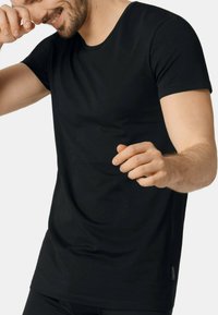Black t-shirt with a round neckline and short sleeves. Made from soft, stretchy fabric, it features a fitted design and side tag detail.