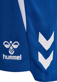 Pantalones cortos deportivos azules con logo blanco de Hummel y dos flechas de chevron blancas en el lateral, fabricados con tejido de malla transpirable.