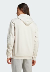 Vaaleanbeige huppari, jossa on naru- ja ribbireunat hihansuissa ja helmassa. Pehmeä, teksturoitu kangas. Päällä harmaat collegehousut, nähtynä takaa.