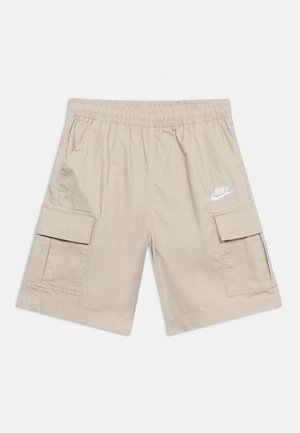Bézs Nike cargo rövidnadrág rugalmas derékpánttal, két nagy oldalsó zsebfedéllel és fehér Nike logóval a bal zseben.