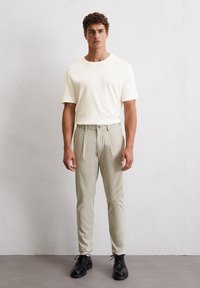 Lichtrommel kortemouwenshirt, beige maatwerk broek, en zwarte veterschoenen. Gladde texturen, klassieke pasvorm en functionele details zijn zichtbaar.
