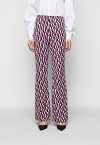 Pantalons évasés avec un motif géométrique audacieux présentant des nuances de rose et de noir sur un fond blanc. Fabriqués en tissu léger.