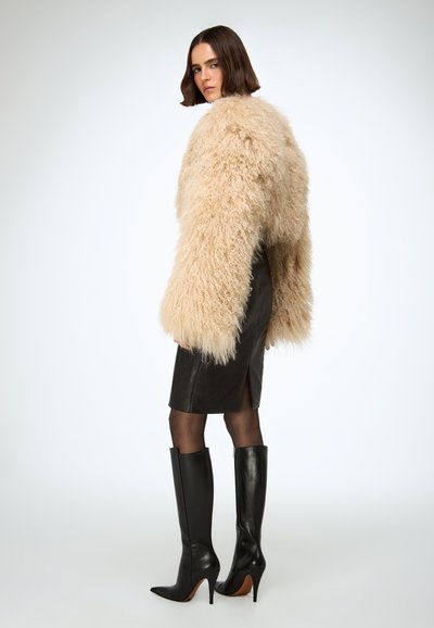 Beige shaggy faux fur jacket with wide sleeves, paired with a fitted black leather skirt and knee-high black stiletto boots.