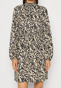 Long-sleeve dress with a high smocked neck, featuring a beige and black abstract animal print pattern. Lightweight fabric with a relaxed fit.