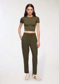 Camicia corta verde oliva e pantaloni a vita alta abbinati, realizzati in un tessuto morbido, abbinati a sneaker di colore chiaro.