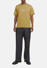 Sennepsgul kortærmet t-shirt med trykt tekst på brystet, parret med løstsiddende mørke denim jeans og sorte chunky-soled støvler.