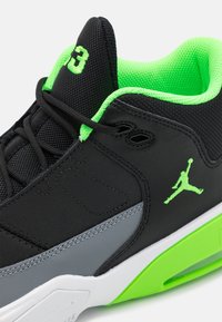 Black athletic shoe featuring a mesh upper with neon green accents, a grey side panel, and a white sole. Includes a visible brand logo.