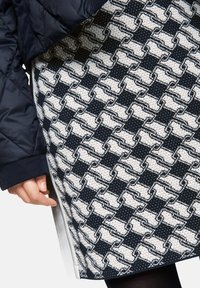 Woven skirt with a navy and white wave pattern, featuring a textured surface and a side slit, partially covered by a puffy jacket.