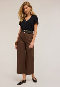 T-shirt noir à col en V avec des embellissements, associé à un pantalon large taille haute marron. Les accessoires comprennent une ceinture texturée et des ballerines noires.