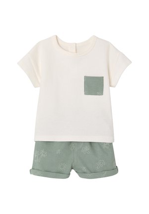 Kurzärmeliges cremfarbenes Hemd mit grünem Brusttaschen kombiniert mit grünen Shorts mit aufgekrempelten Bündchen und dezenten Blattmustern.