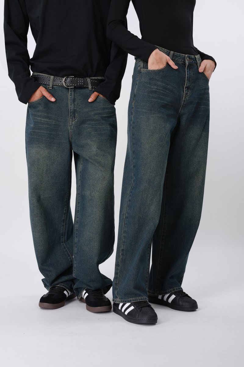 Τζιν μπλε με φαρδύ πόδι και ανοιχτή πλύση, σε συνδυασμό με μαύρα μακρυμάνικα πουκάμισα και μαύρα παπούτσια με λευκές ρίγες, φορεμένα σε casual στιλ.