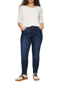 Granatowe dżinsy o prostym kroju, w zestawieniu z białą koszulą z długim rękawem. Obuwie charakteryzuje się połączeniem beżowych i czarnych akcentów.