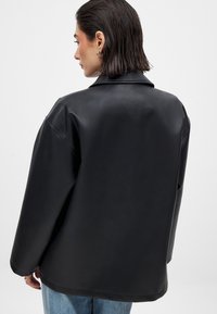 Giubbotto di pelle nera con un ampio colletto, vestibilità oversize e texture liscia. La vista posteriore mette in mostra spalle basse e cuciture minime.
