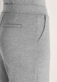 Nahaufnahme von hellgrauen Hosen mit vorderen und hinteren Paspeltaschen, die den strukturierten Stoff und die Seitennähte zeigen.