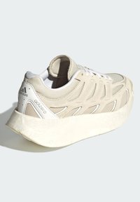 Beige sportssko med ovandel i mesh och mocka, vita accenter och en tjock strukturerad sula med en distinkt böjd design.