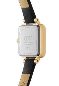 Gold stainless steel watch with a square case, black leather strap, and a beige accent on the strap. Back features engraved details and serial number.