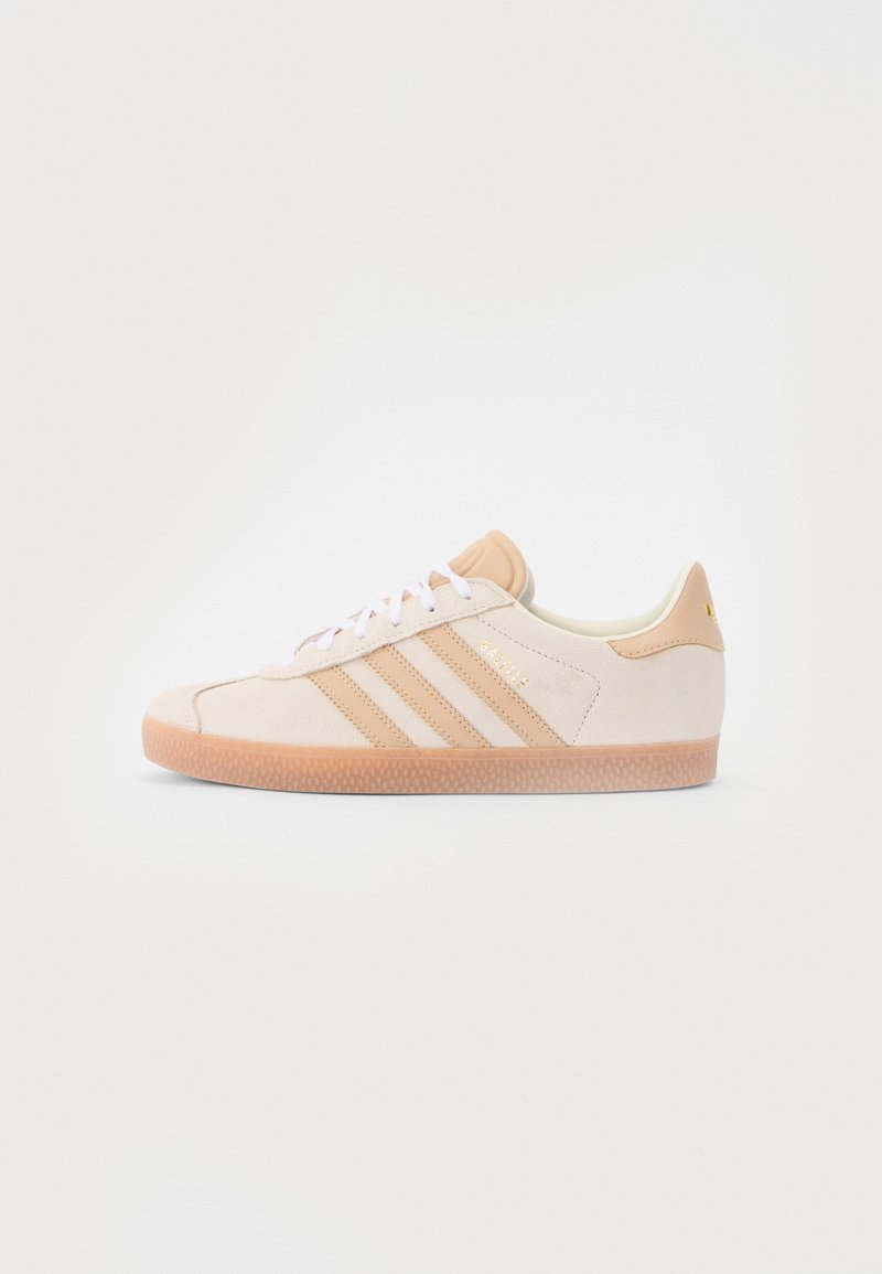 Ljust rosa mocka sneakers med texturerad gummisula, vita snören och tre matchande ränder. Har detaljer i guld och en låg profil.