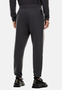 Pantaloni jogger grigi in materiale morbido, con vita elastica e dettagli laterali. Abbinati a sneakers nere, che mostrano una linea elegante.