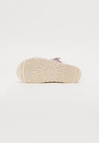 Semelle de chaussure beige clair avec des motifs géométriques de bande de roulement et un design circulaire au centre, présenté sur un fond blanc.