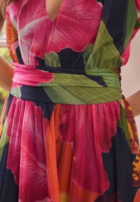 Blumenkleid mit großen pinken und grünen Blumenmustern auf dunklem Grund. Verfügt über eine taillierte Silhouette und eine geraffte Rockstruktur.