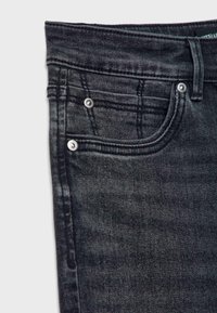Gros plan sur la partie avant supérieure d'un jean en denim gris foncé montrant la ceinture, la boucle de ceinture et la poche avant avec des rivets métalliques.