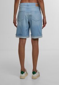 Shorts en denim bleu clair avec ourlets retroussés, dotés de deux poches arrière et d'une étiquette en cuir brun avec logo sur la ceinture.