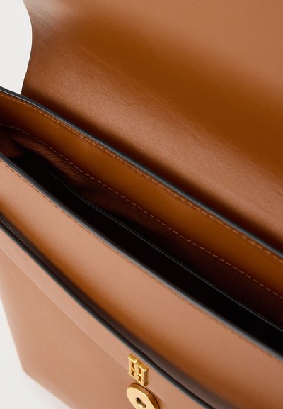 Τσάντα από δέρμα ταμπά με ανοιχτό καπάκι, αποκαλύπτοντας εσωτερικό με μεγάλο χώρο και χρυσό κυκλικό κούμπωμα στο μπροστινό μέρος.