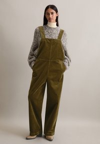 Olijfgroene corduroy salopettes met een losse fit, wijde benen en stevige schouderbanden. Gecombineerd met een dikke, gestructureerde grijze trui.