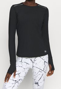 Svart långärmad sporttopp med kontrasterande vit söm, texturerad tyg och böjd fåll. Matchad med vita leggings med ett svart marmor-mönster.