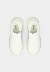 Λευκά παπούτσια τύπου slip-on με υφή στο πάνω μέρος, στρογγυλεμένη μύτη και παχιά σόλα από καουτσούκ. Ο σχεδιασμός χαρακτηρίζεται από ελαφρύ, μινιμαλιστικό στυλ.