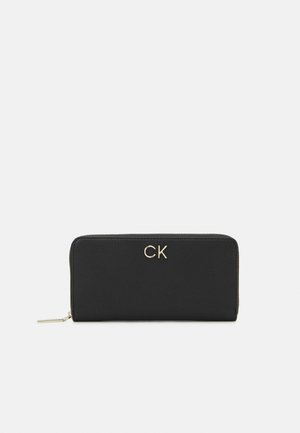 Črn usnjen denarnica z teksturirano površino, z zlatim "CK" logotipom spredaj in z zadrgo ob robu.