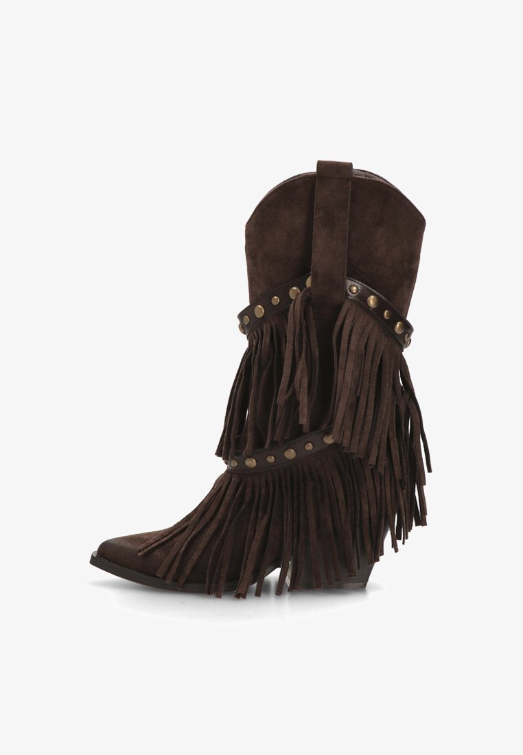 Botín de ante marrón con detalle de flecos, adornos de tachuelas, punta puntiaguda y tacón cuña. Textura suave y elementos decorativos que realzan el diseño.