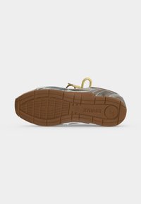Chaussure vue du côté de la semelle avec une semelle extérieure en caoutchouc texturée marron, des lacets visibles et un texte de marque en bas.