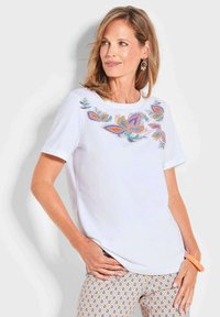 T-shirt blanc à manches courtes orné de motifs floraux brodés colorés autour de l'encolure. Tissu doux avec une coupe décontractée.