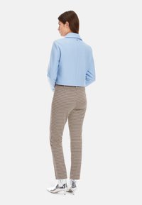 Hellblaues, kurz geschnittenes Jacket mit Kragen, kombiniert mit braunen Hahnentrittmuster-Hosen und glänzenden silbernen Ankle Boots.