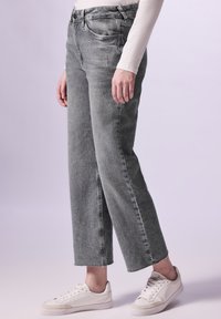 Jean taille haute gris clair avec une coupe droite, comportant des déchirures subtiles et des ourlets effilochés, associés à des baskets blanches.
