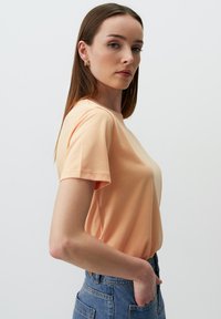 Różowo-brzoskwiniowa bawełniana koszulka z okrągłym dekoltem, krótkimi rękawami i luźnym krojem, w połączeniu z jasnoniebieskimi spodniami dżinsowymi o wysokim stanie.