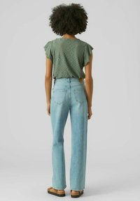 Blusa verde a pois con maniche a farfalla, abbinata a jeans a gamba dritta a vita alta di colore azzurro e sandali neri flat.