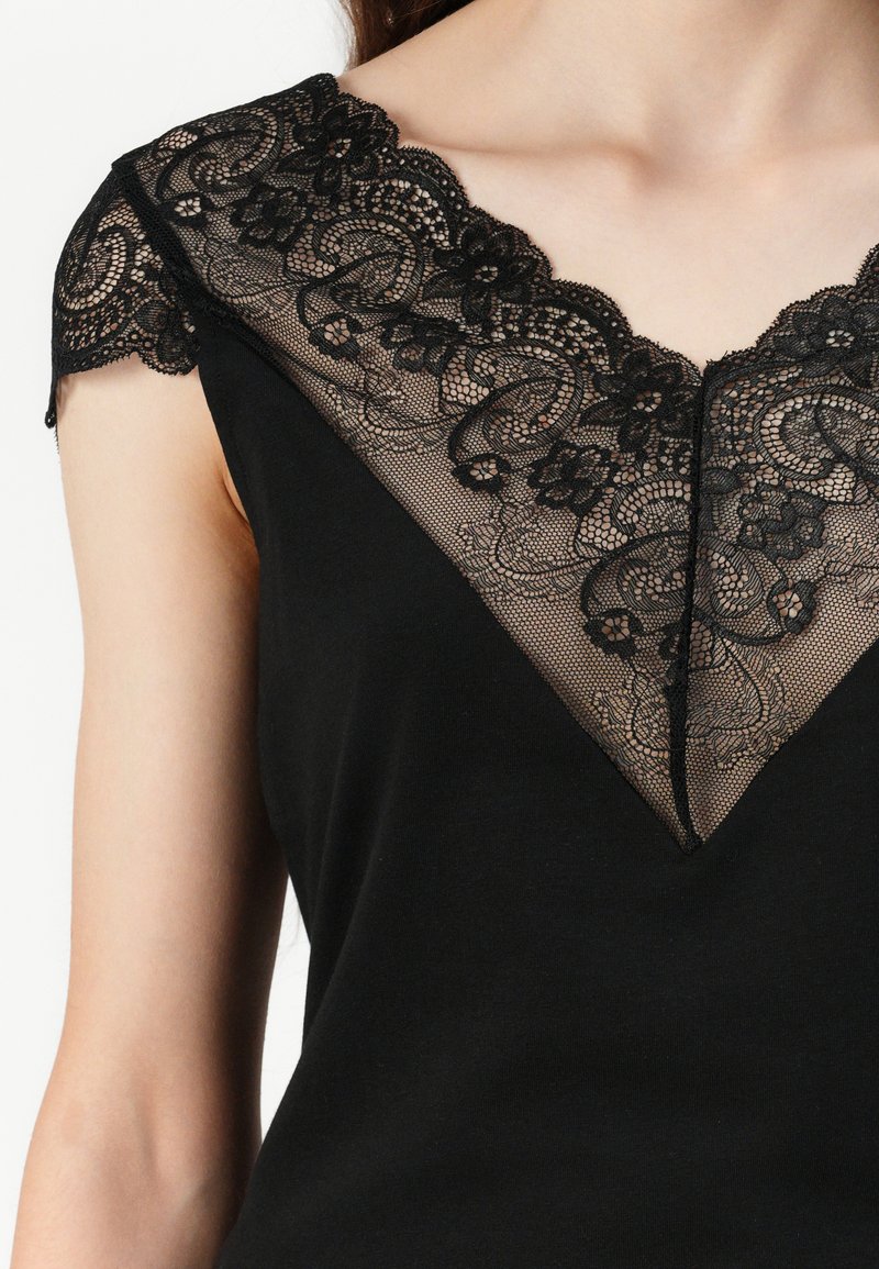 Czarny top z dekoltem w kształcie litery V, ozdobiony misternym czarnym koronkowym wykończeniem. Koronka ma kwiatowe wzory oraz falbaniasty brzeg.