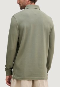 Polo a maniche lunghe in verde oliva, realizzata in tessuto morbido, con collo classico e spacchi laterali sull'orlo per facilitare i movimenti.