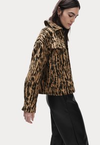 Veste en imprimé animal brun et noir avec un col, des poches avant et une coupe courte. Le tissu texturé ajoute de la dimension au design.