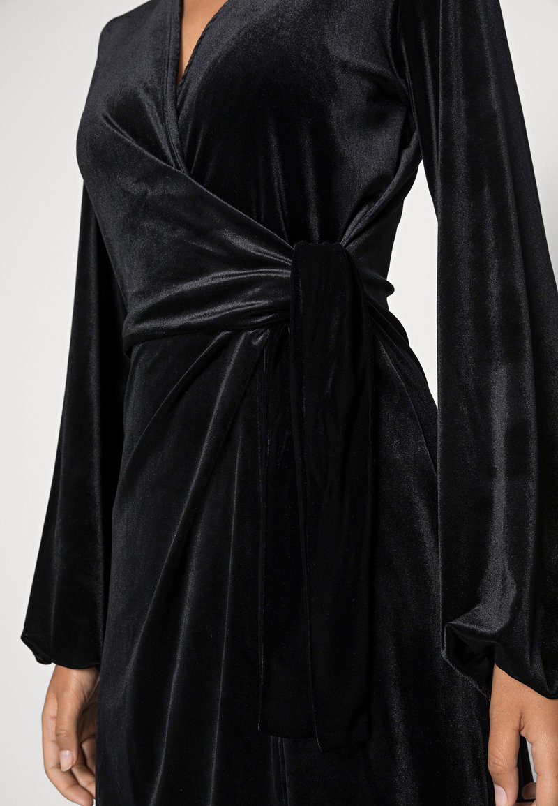 Schwarzes Samt-Wickelkleid mit langen Ärmeln, das eine Front-Knotendetail und eine weiche, glänzende Textur aufweist, die elegante Drapierungen betont.